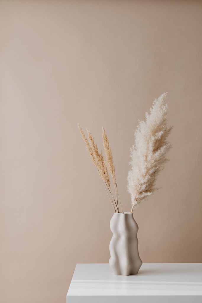 Elegant pampas grass in a sculpted ceramic vase on a white table, showcasing minimalist style.